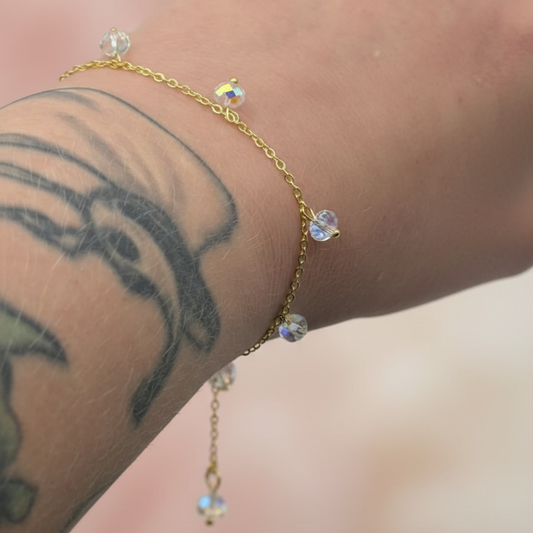 Gold chain crystal charm bracelet on arm on a light pink background 