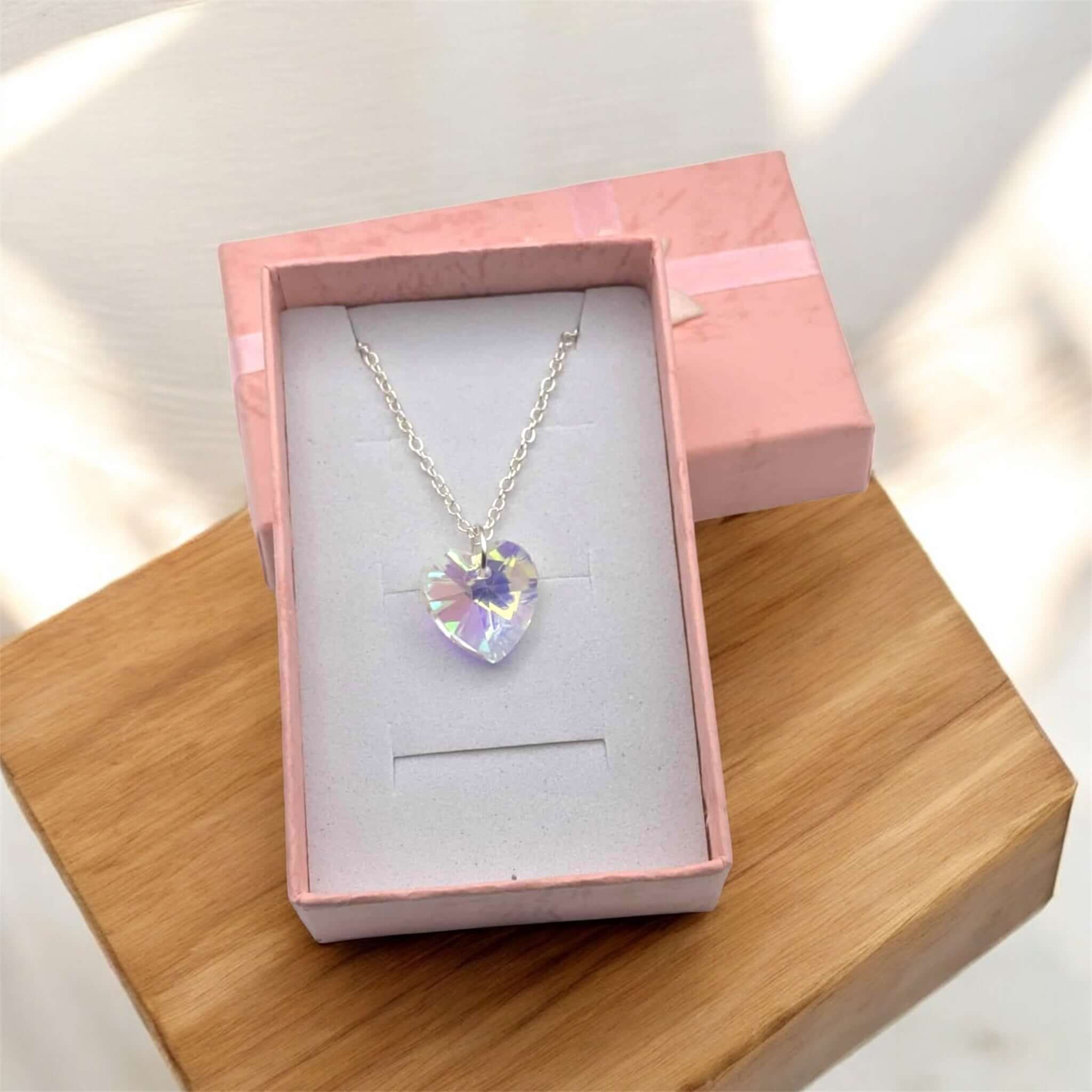 Necklace with a heart-shaped crystal pendant in a pink box on a wooden surface