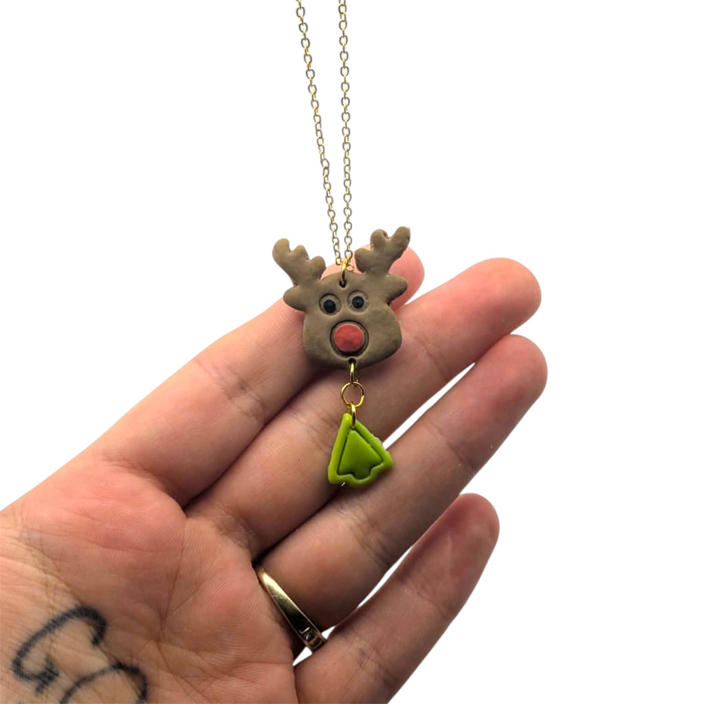 Hand holding a reindeer-shaped necklace with a green tag on a white background
