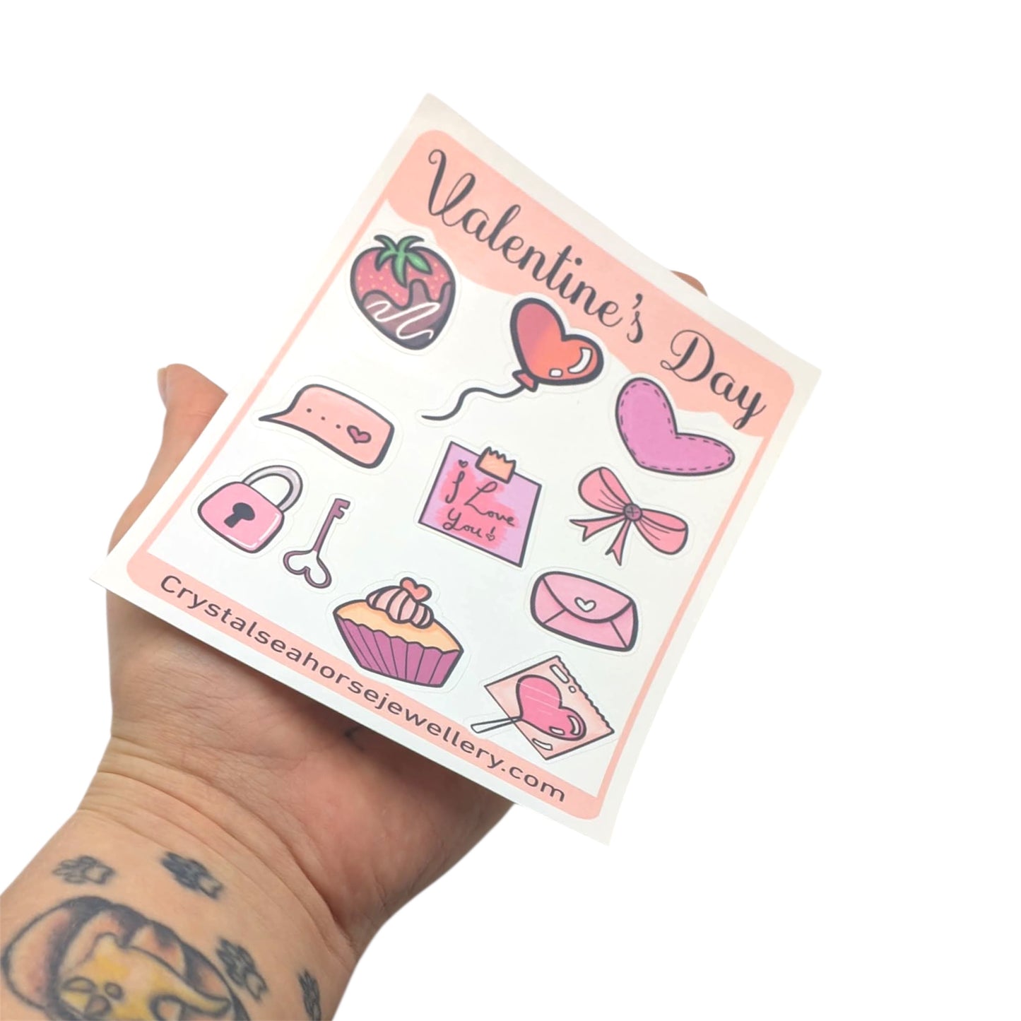 Valentine's Day themed sticker sheet held by a person with tattoos on a white background