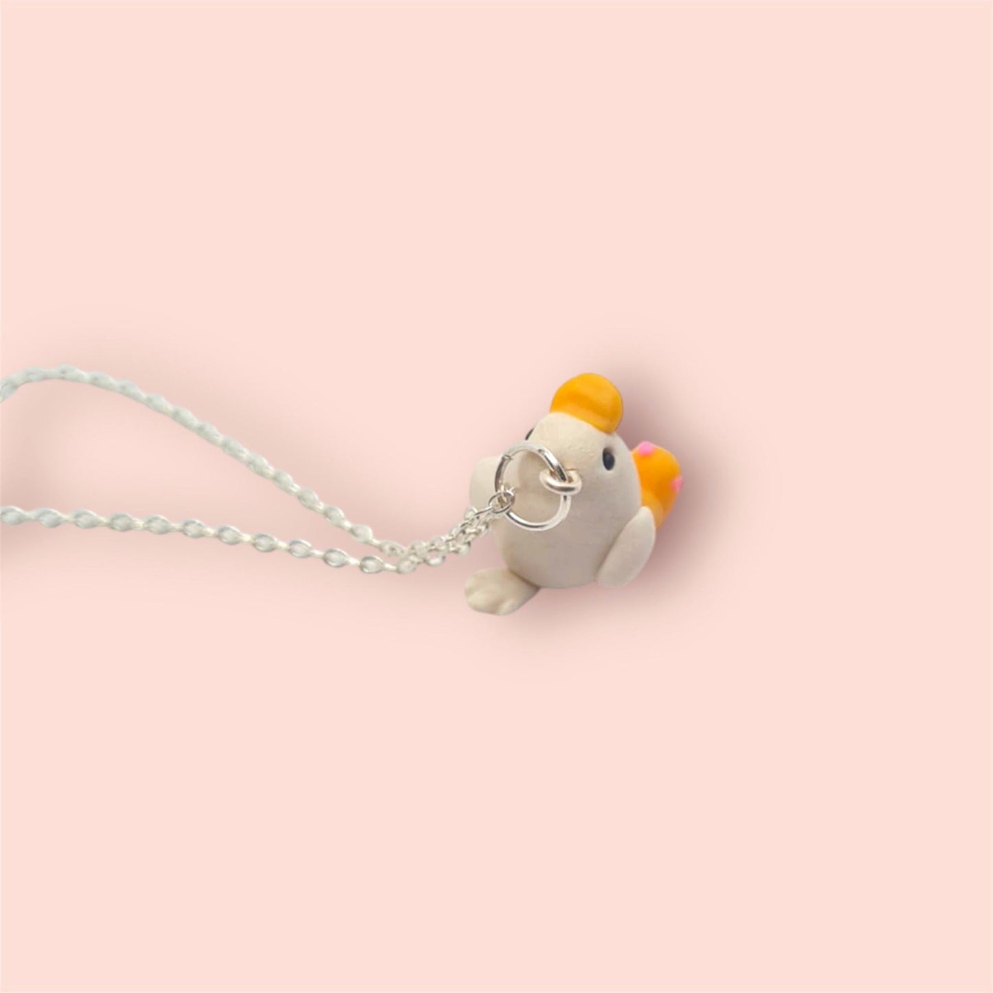 Small bird-shaped charm on a chain against a light pink background