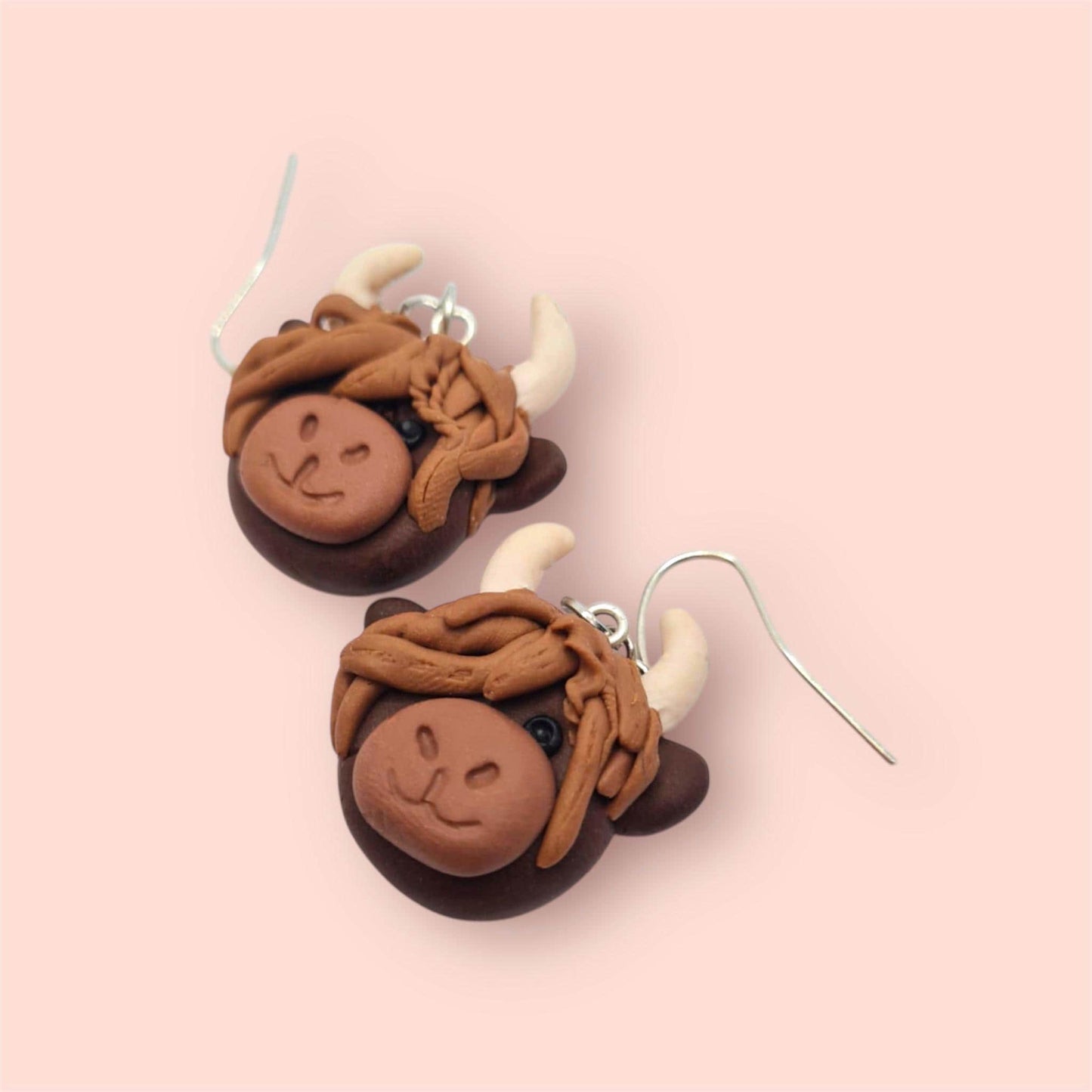 Pair of brown cow-shaped earrings on a pink background