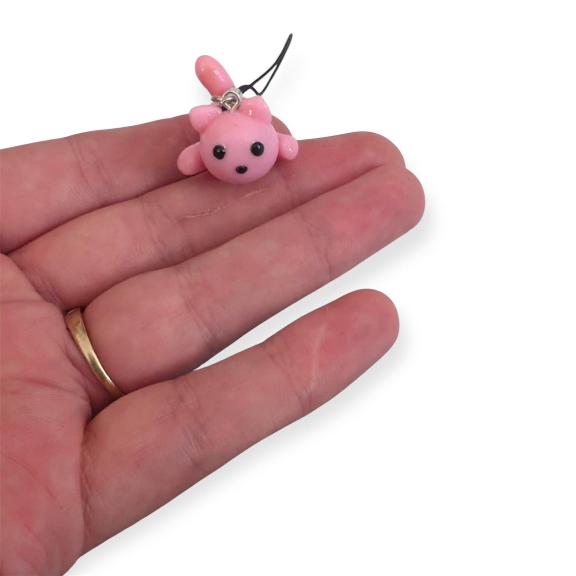 Small pink cat shaped charm held in a hand on a white background