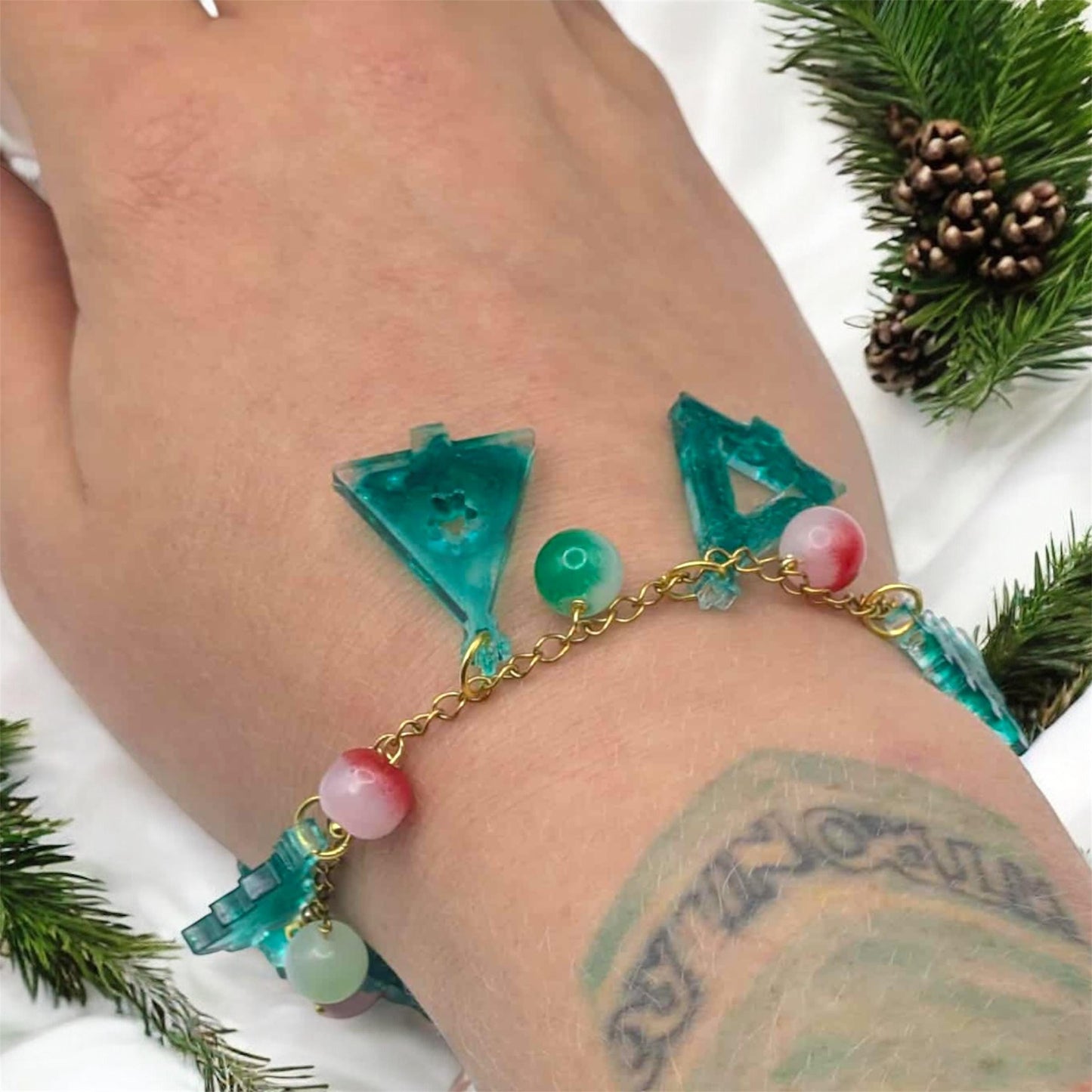 Bracelet with green and pink beads on a wrist with a tattoo, surrounded by greenery.