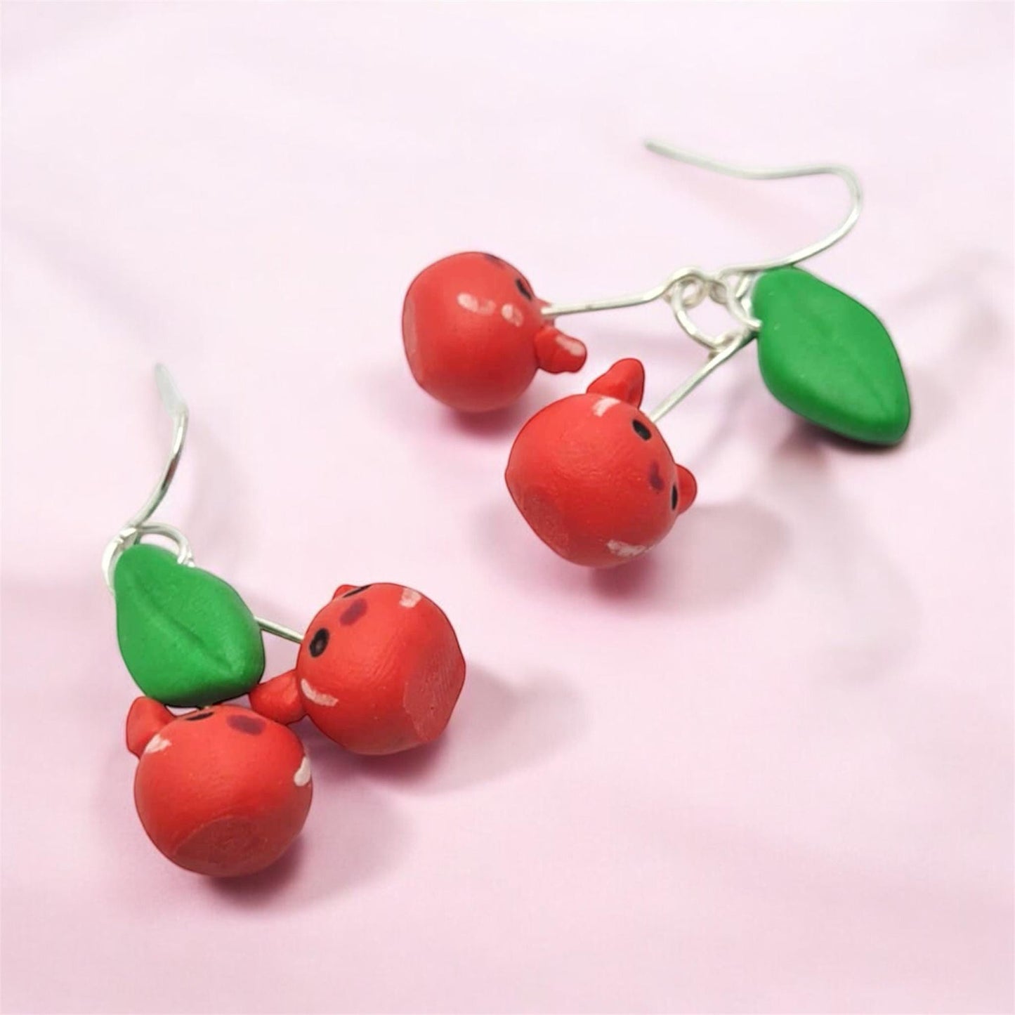 Cherry-themed earrings on a pink background