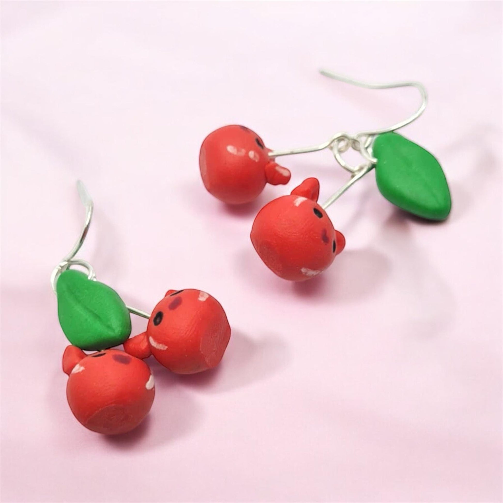 Cherry-themed earrings on a pink background