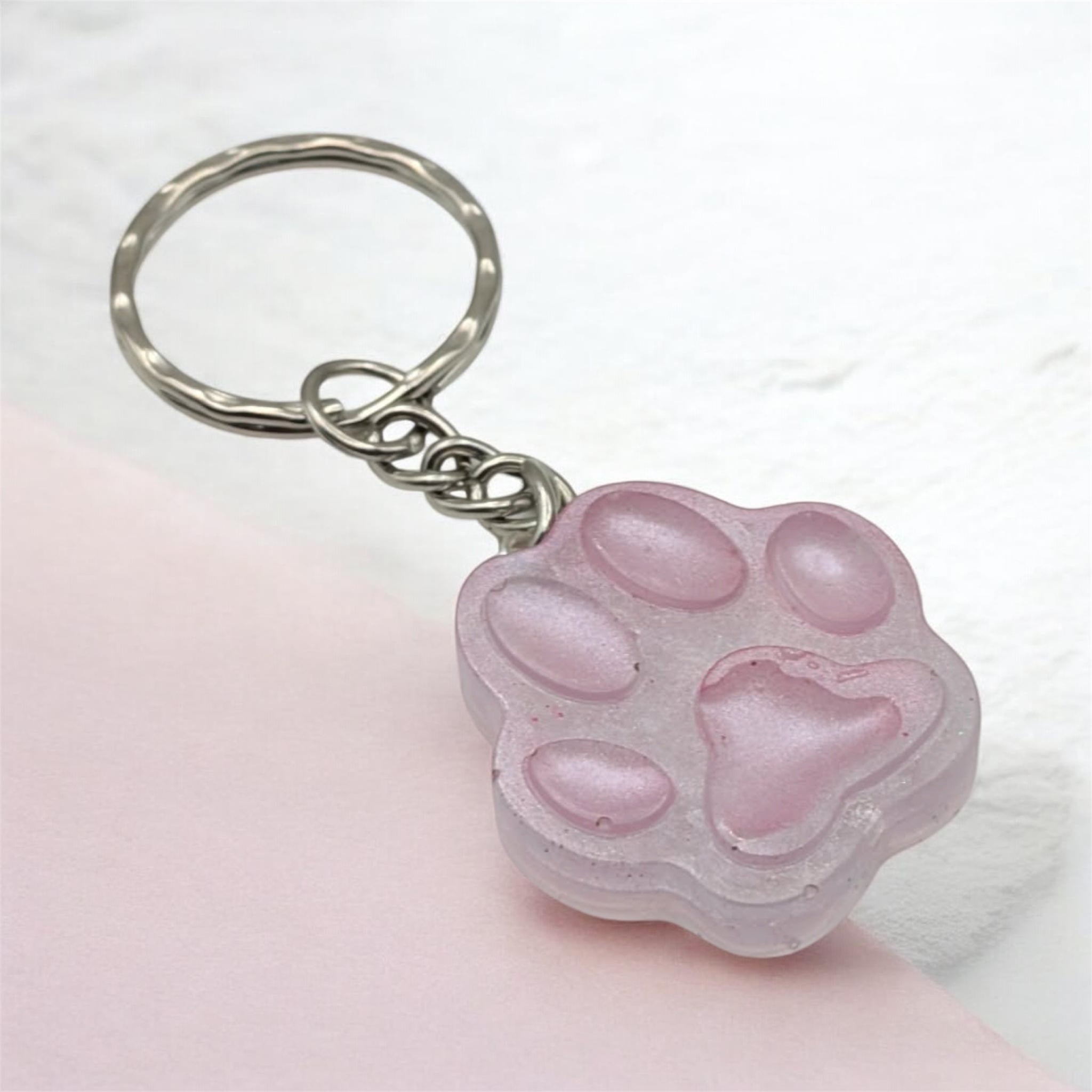 Pink resin paw print keychain on light pink background, handmade in the UK