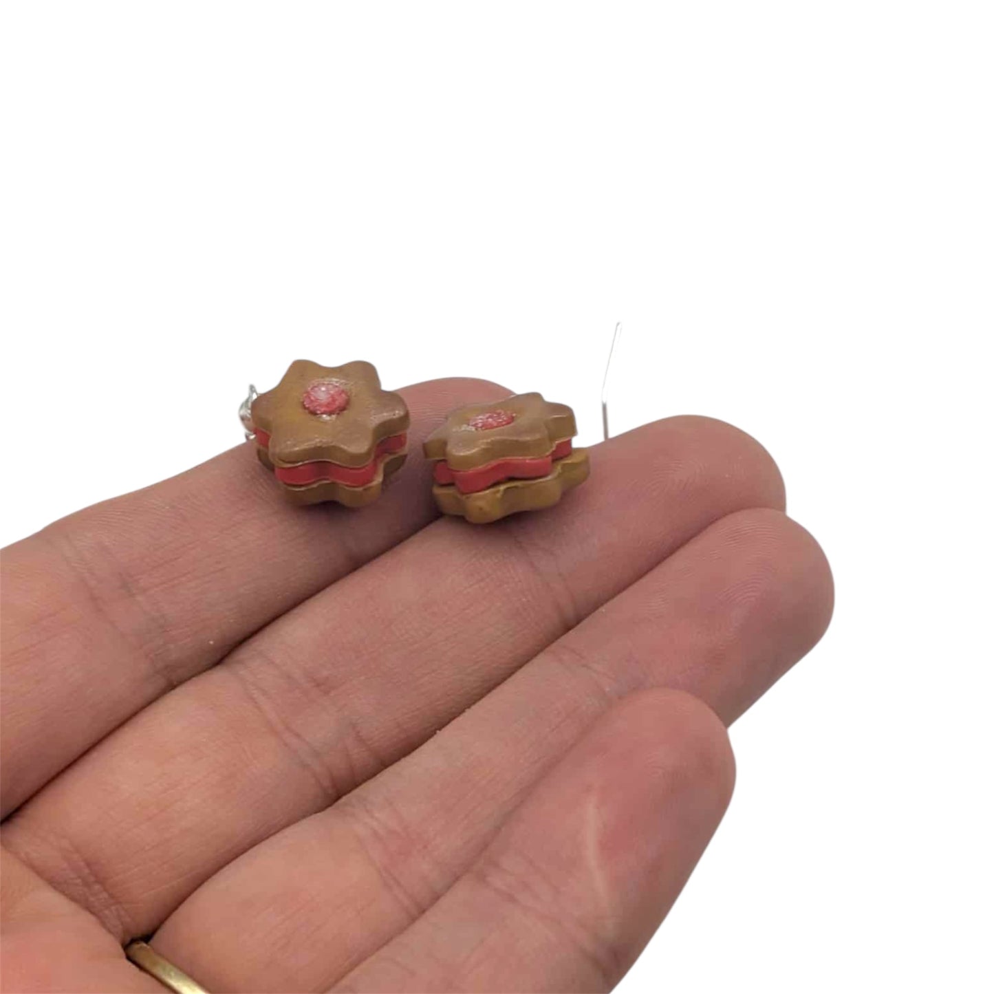 Small star-shaped earrings with pink centers held between fingers on a white background