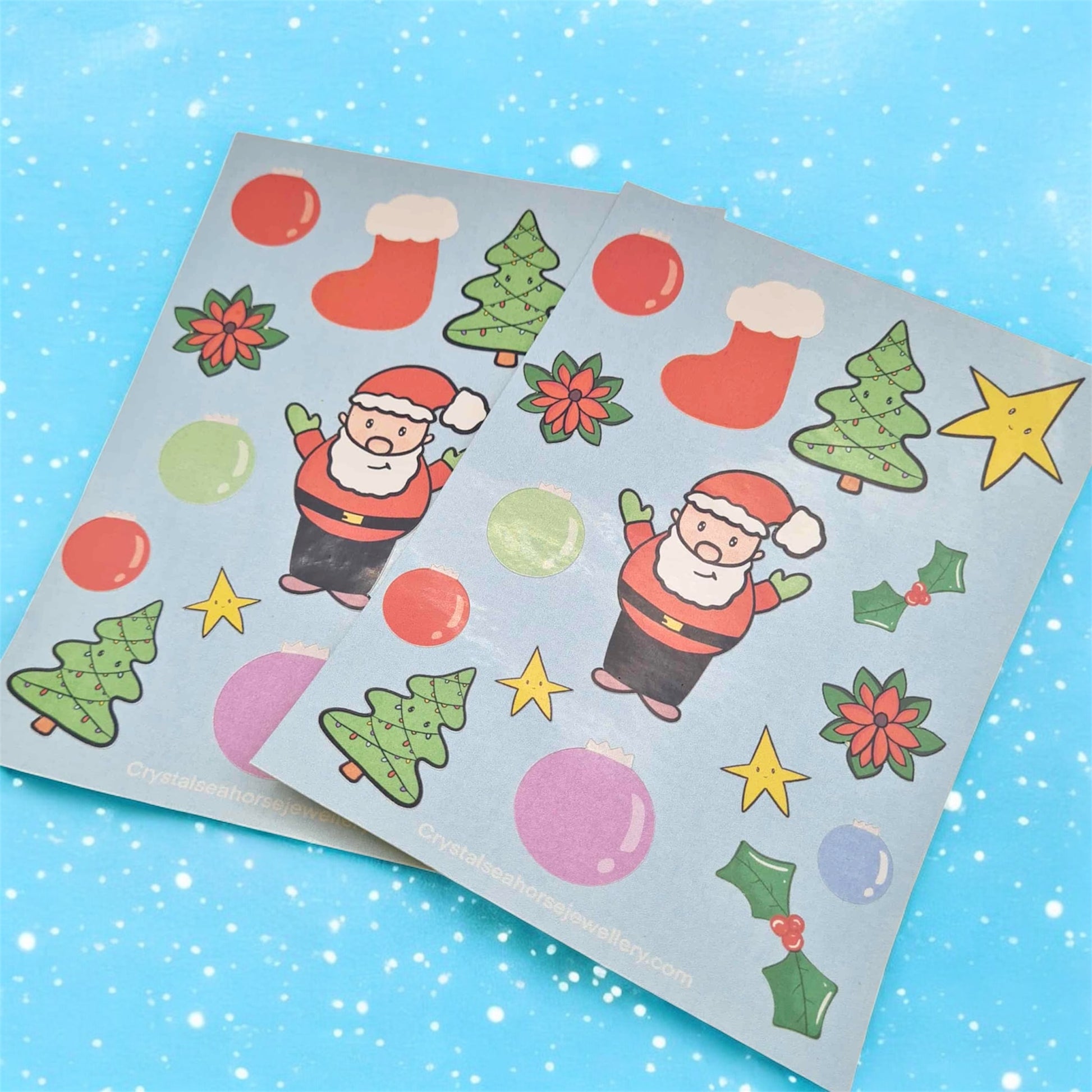 Flat lay of Christmas sticker sheets side by side on a blue snowy background 