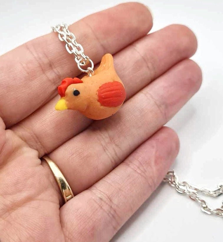 Chicken-shaped pendant on a chain held in a hand with a white background