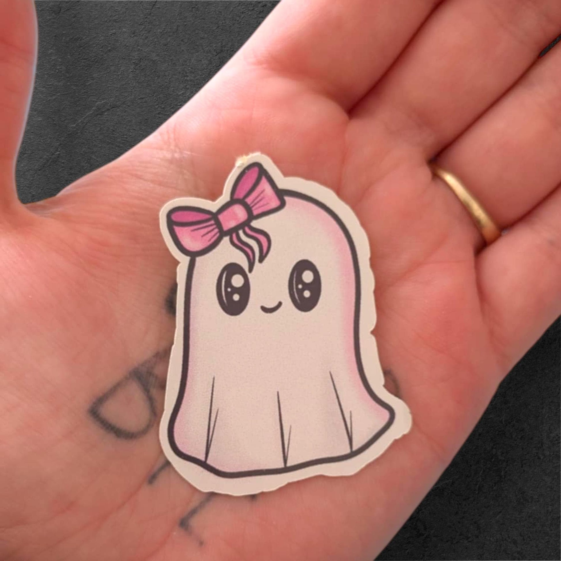 Cute ghost sticker with a pink bow held in a hand.