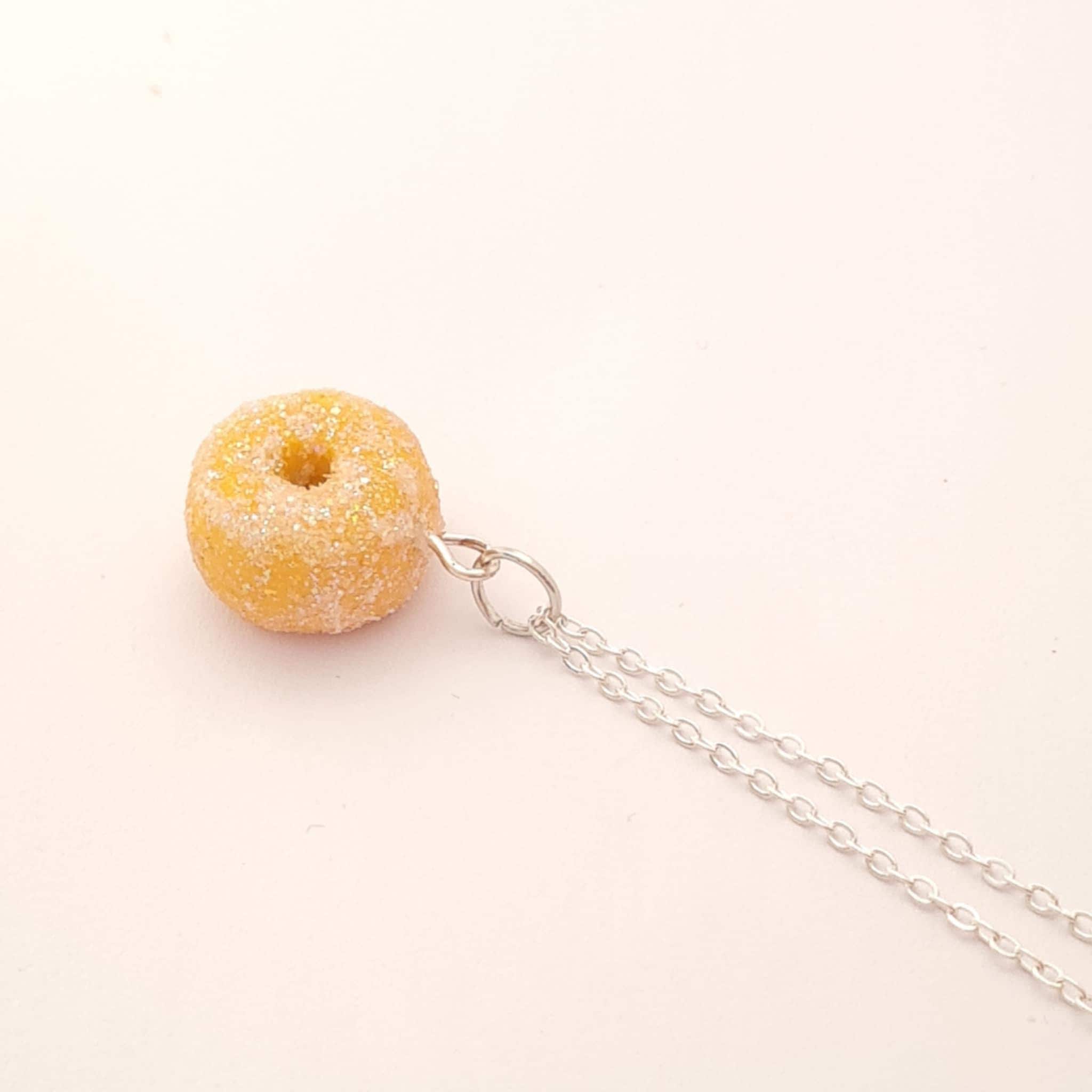 Donut-shaped pendant on a chain against a light pink background