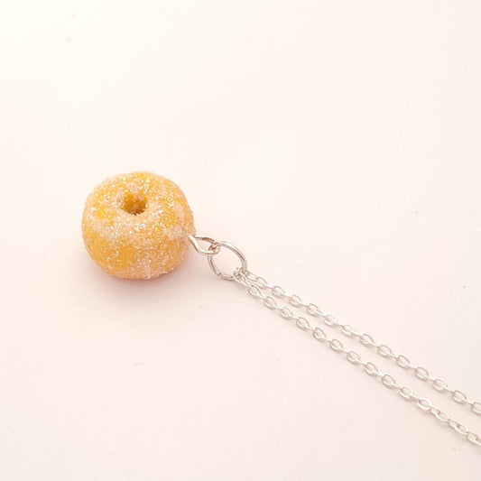 Donut-shaped pendant on a chain against a light pink background