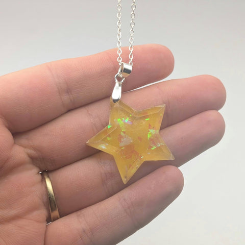 Star-shaped pendant on a chain held in a hand against a neutral background