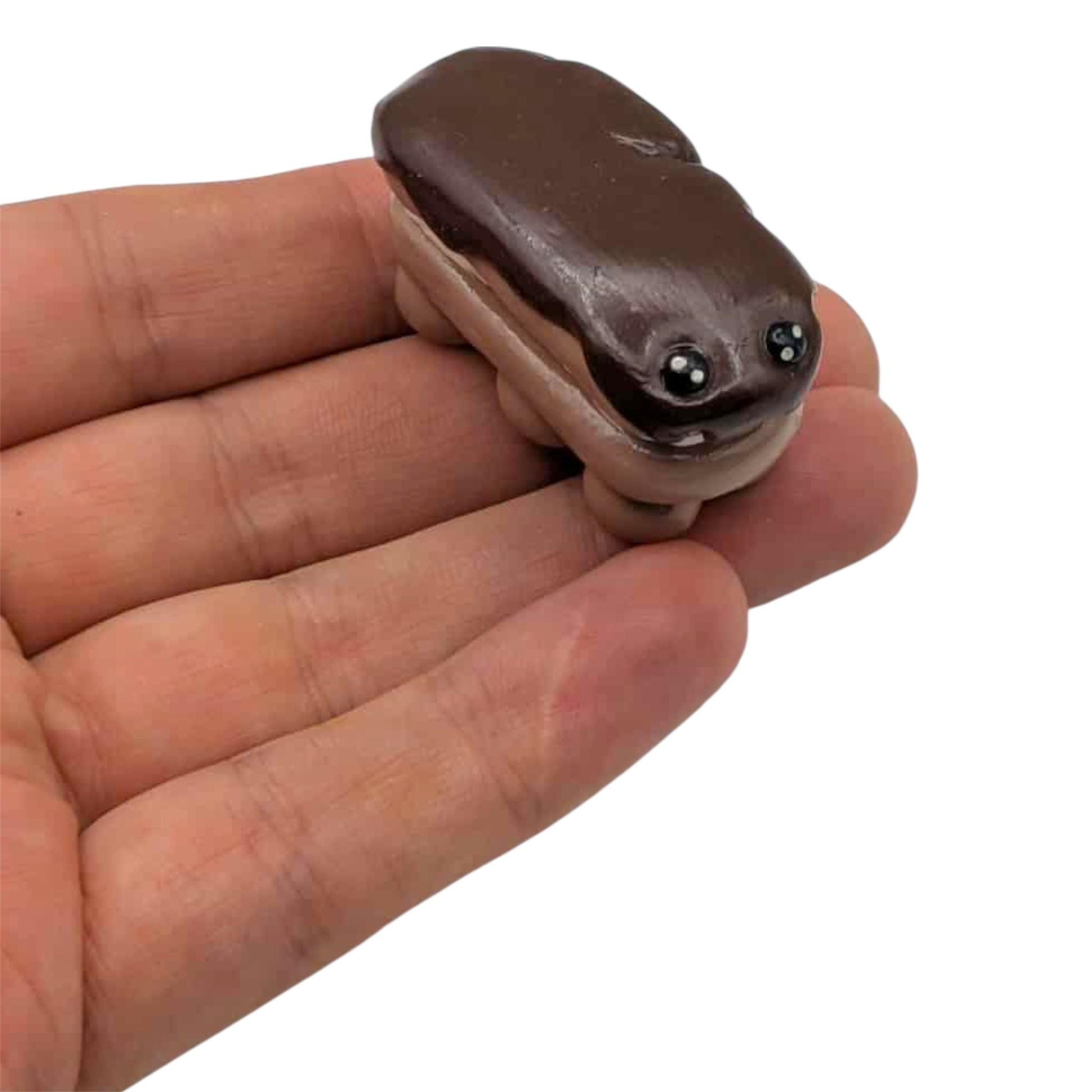 Small clay cake sculpture held in a hand on a white background