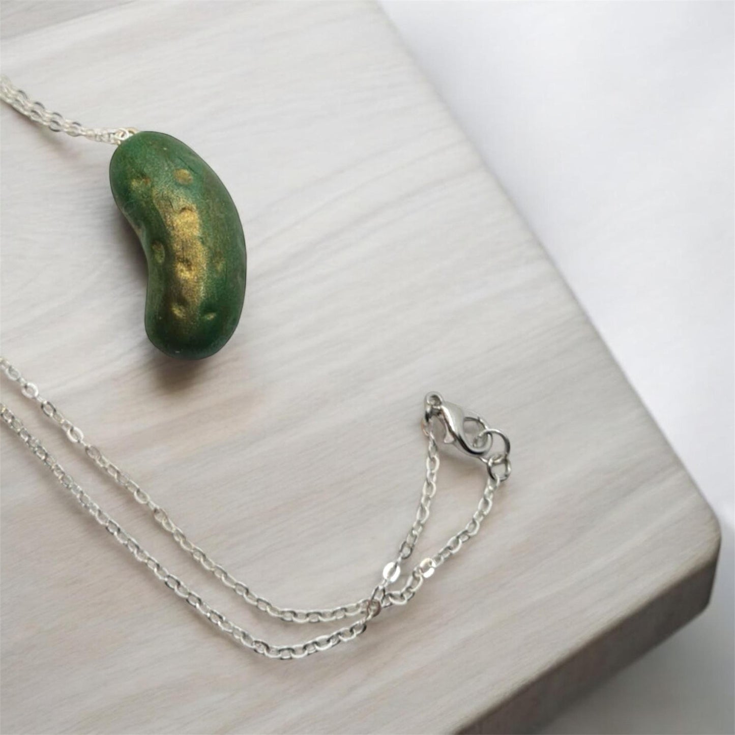 Silver chain necklace with a green pendant on a light wooden surface