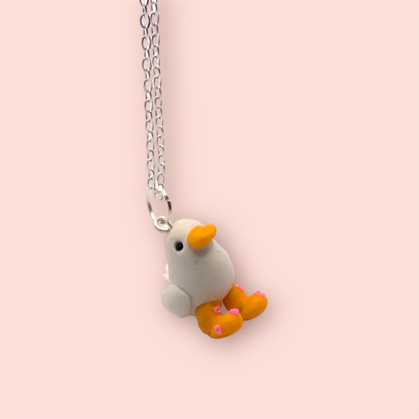 Necklace with a small duck-shaped pendant on a pink background