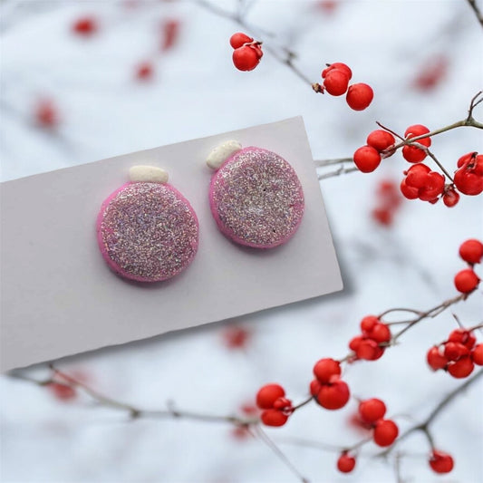 Pink glittery earrings on a white card with red berries in the background