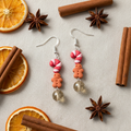 Pair of earrings with candy cane and gingerbread design on a decorative background with oranges and cinnamon sticks.