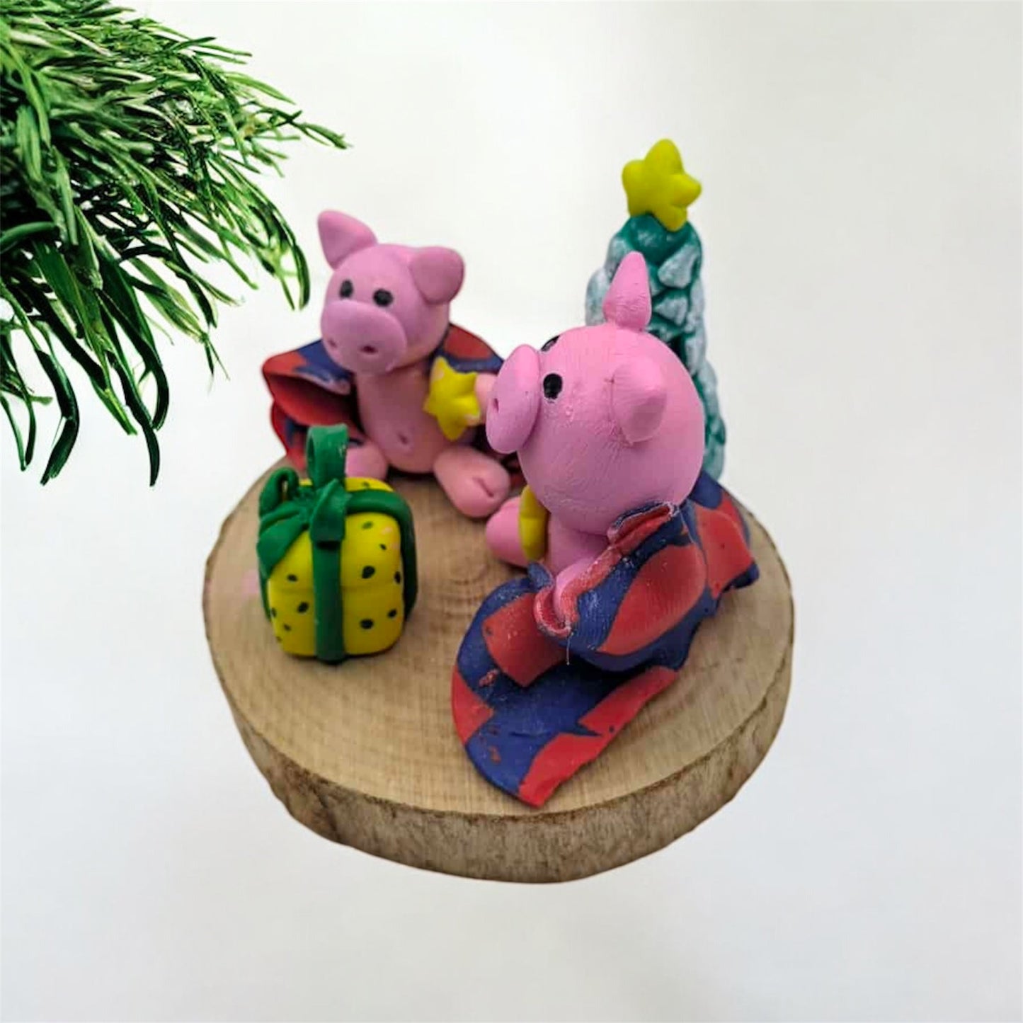 Two pink pig figurines with colorful outfits on a wooden base with a white background