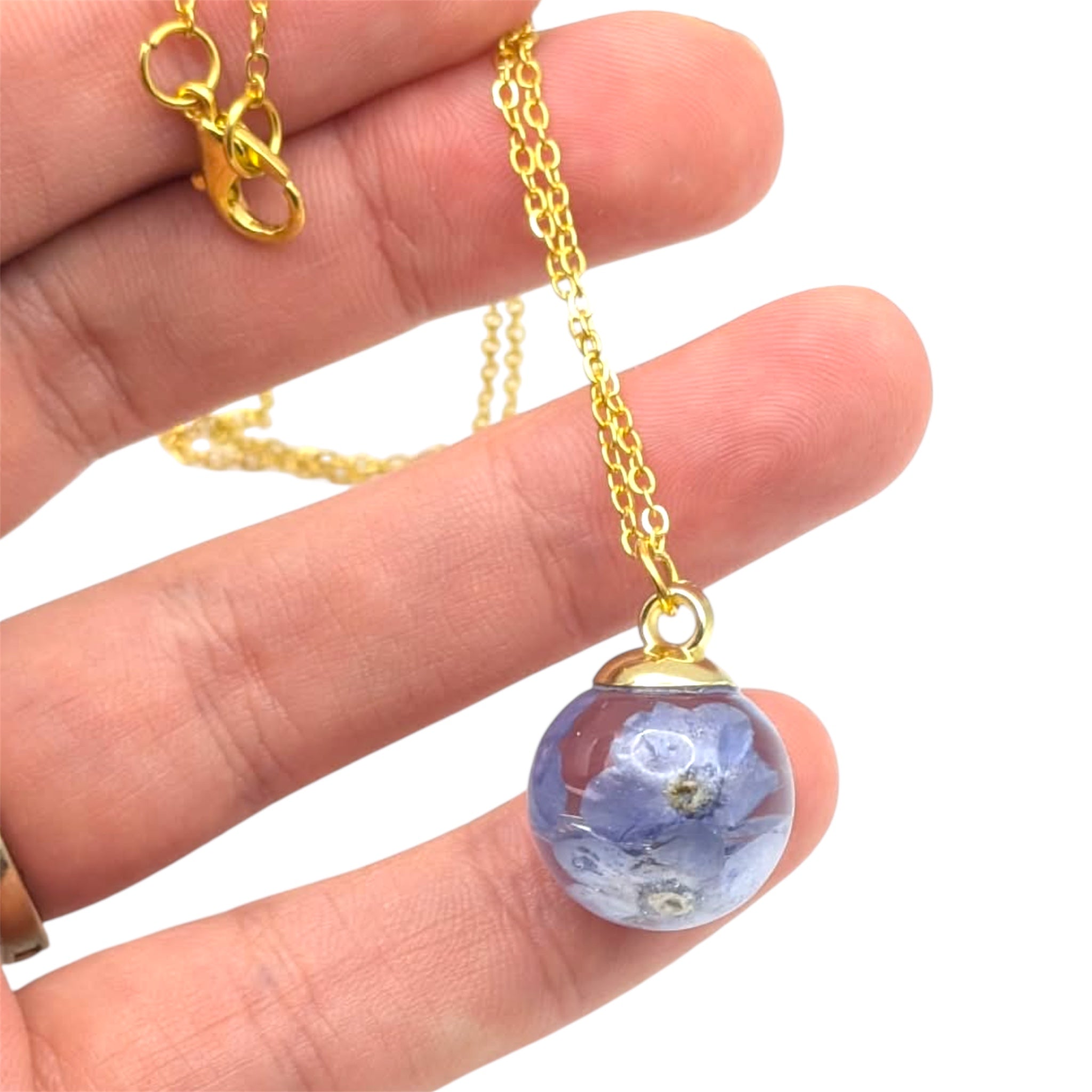 Gold necklace with a blue floral pendant held between fingers on a white background