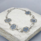 Bracelet laying flat on white surface with blue background, handmade resi. Jewellery with real pressed forget me not flowers 