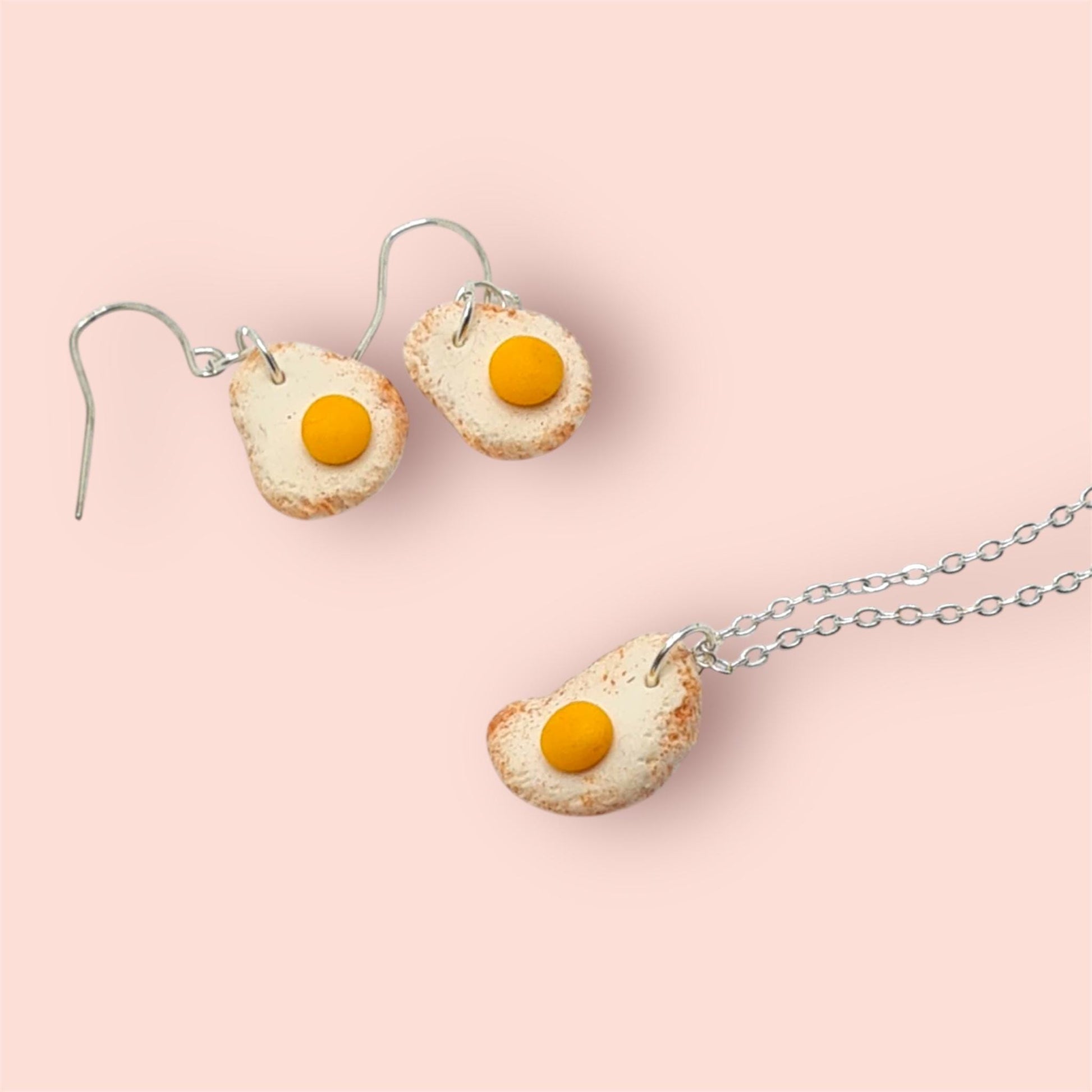 Fried egg-shaped earrings and necklace on a pink background