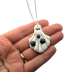 Hand holding a ghost-shaped pendant necklace with a white background
