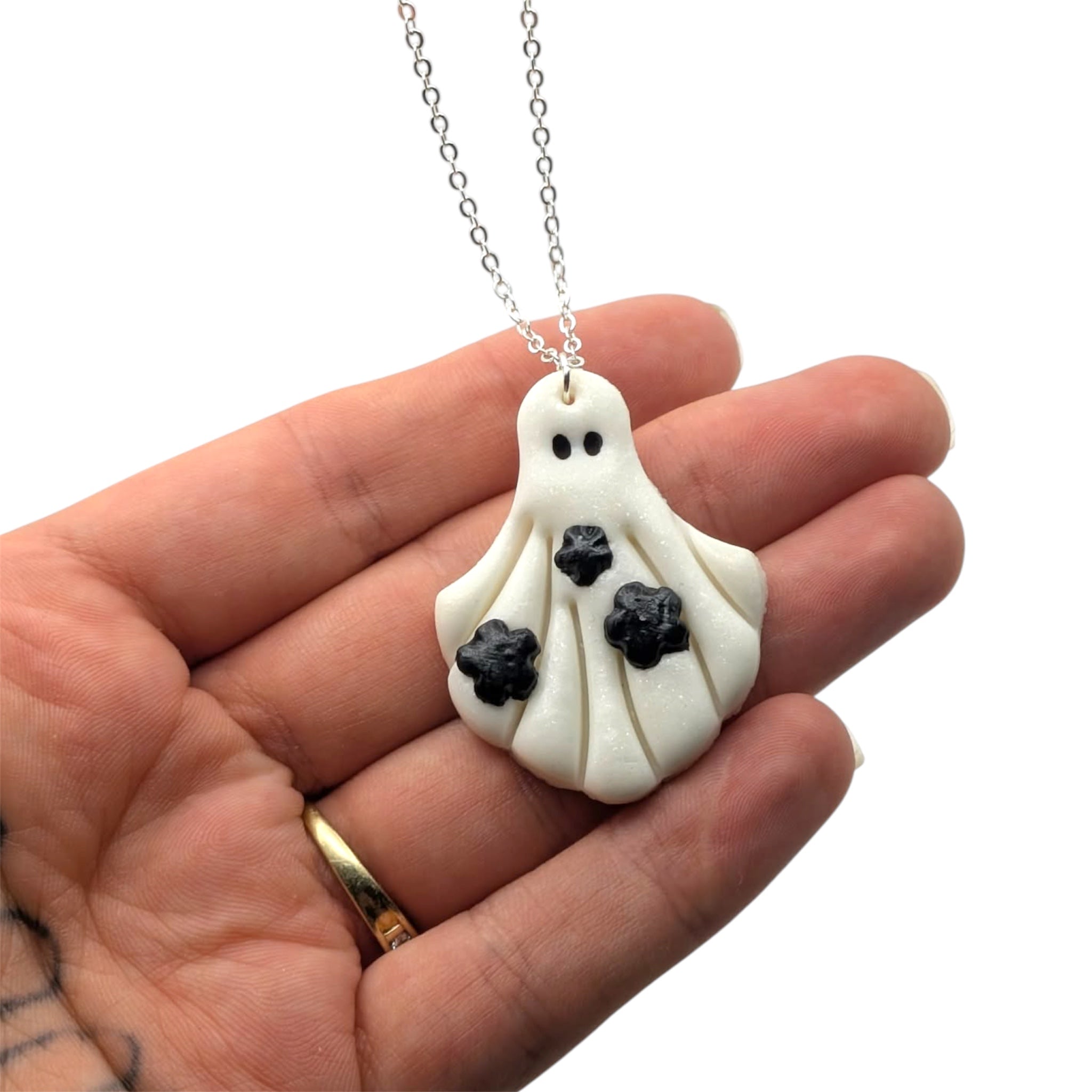 Hand holding a ghost-shaped pendant necklace with a white background