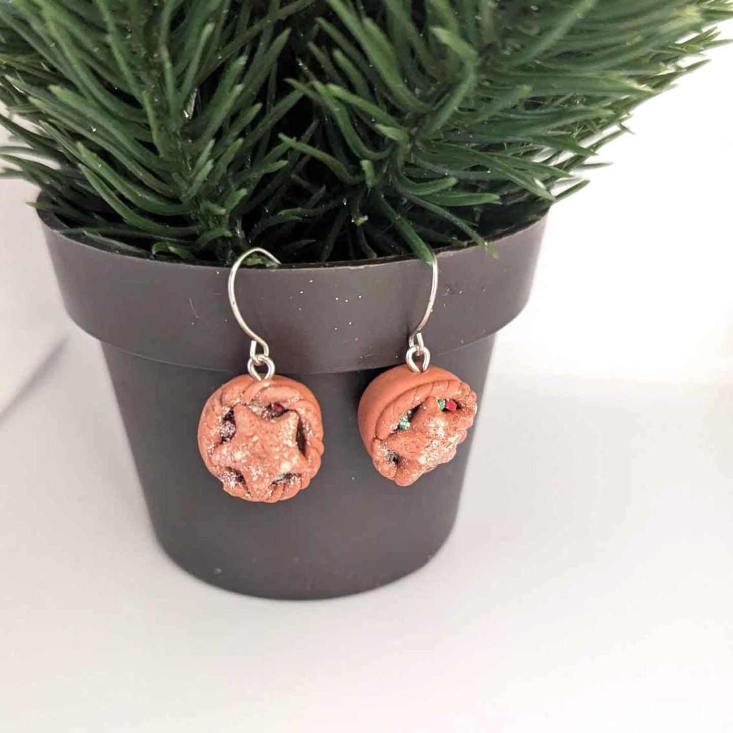Pair of beige earrings hanging from a pot with festive greenery
