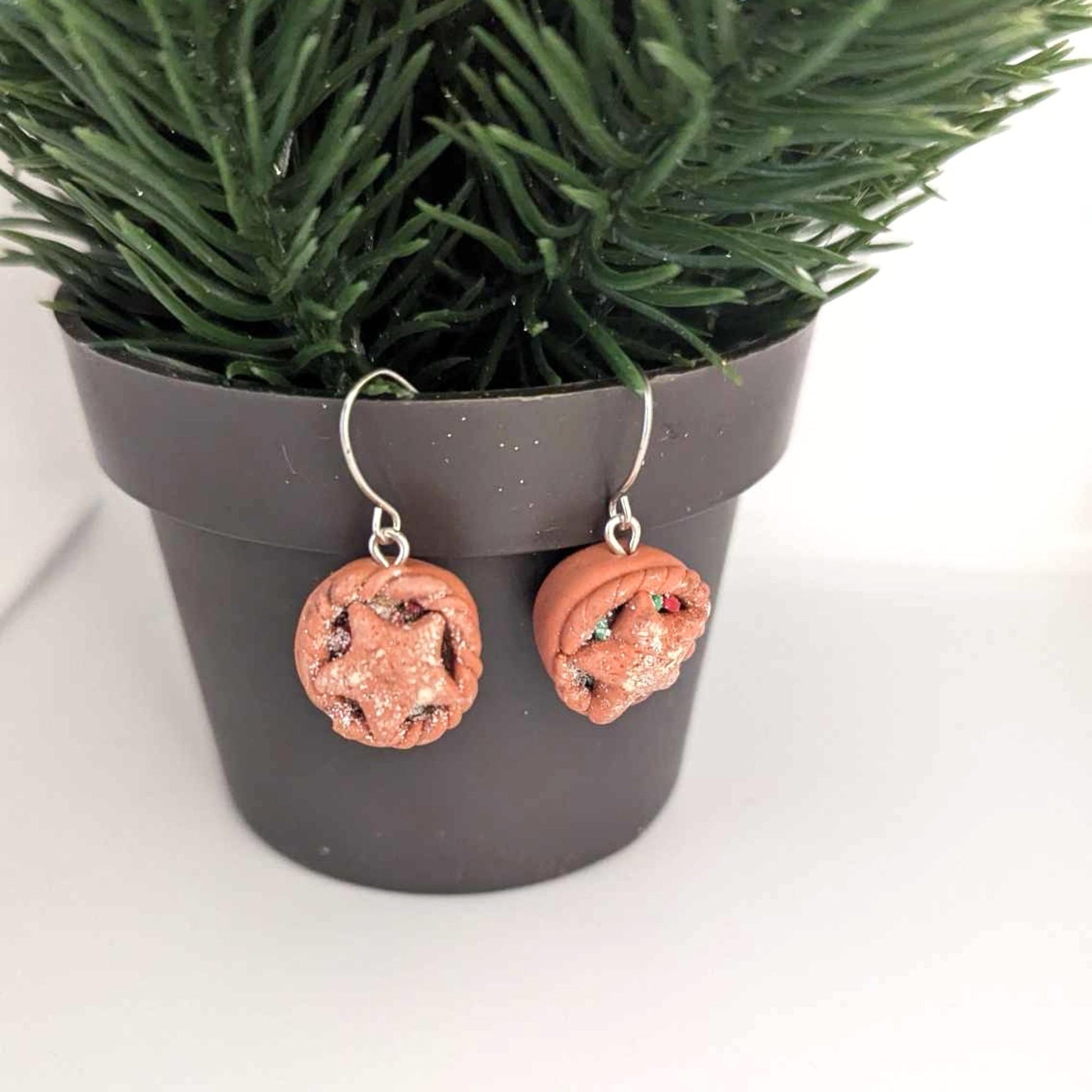 Pair of beige earrings hanging from a pot with festive greenery