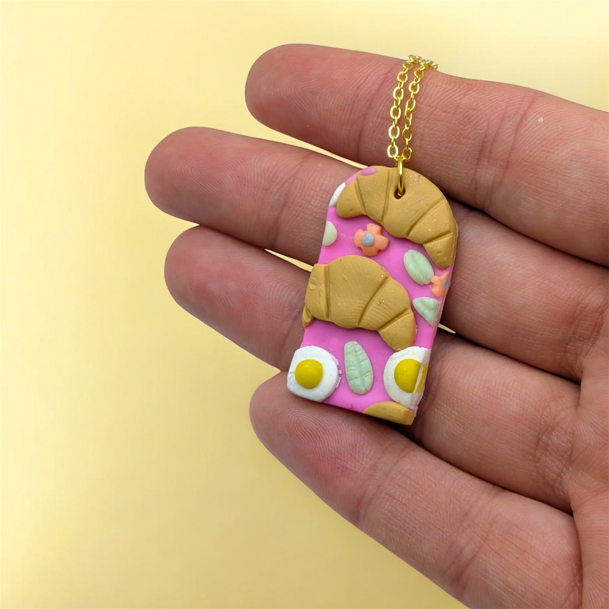 Hand holding a colourful arch shaped pendant with a gold chain against a yellow background