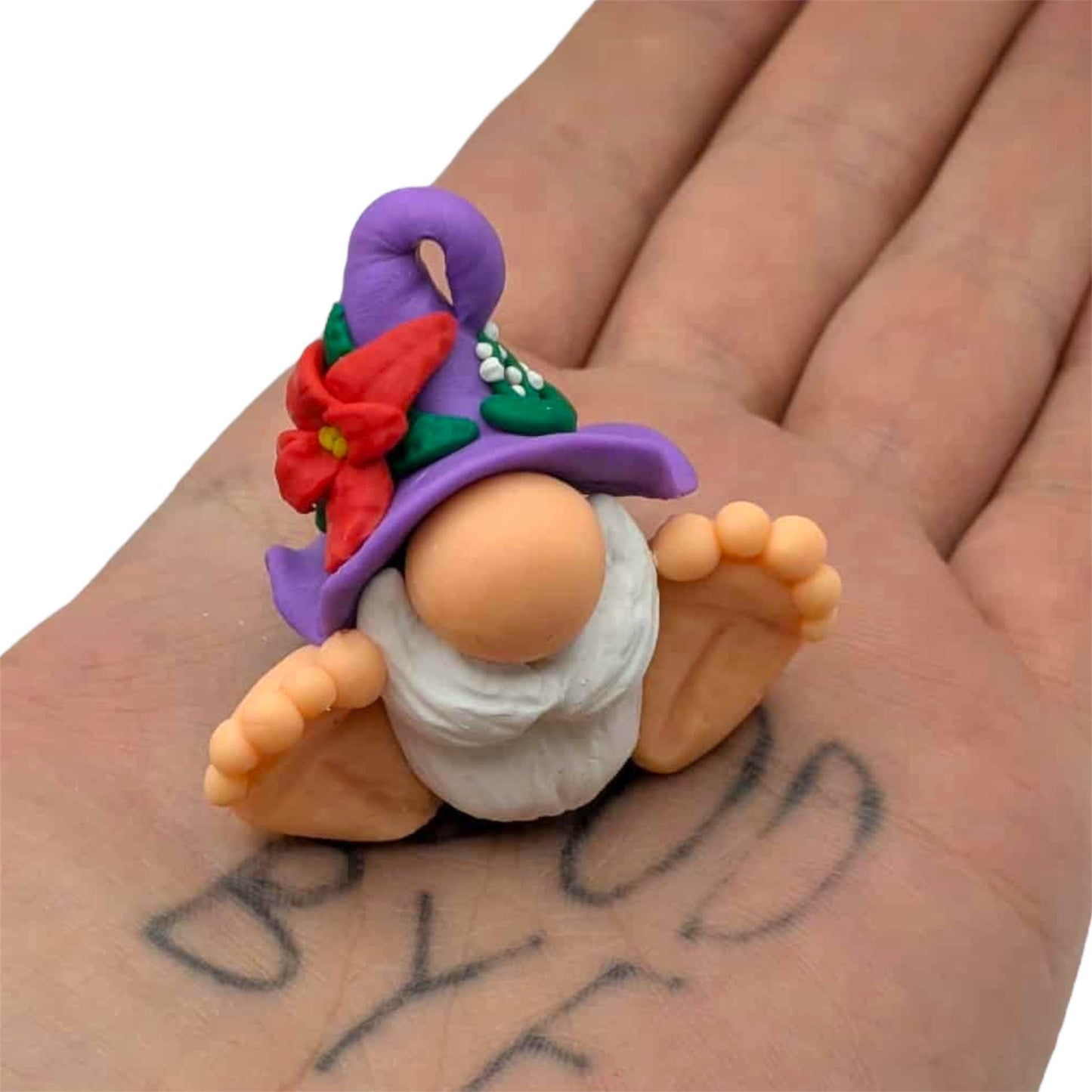 Small gnome figurine with a purple hat held in a hand with visible tattoos.