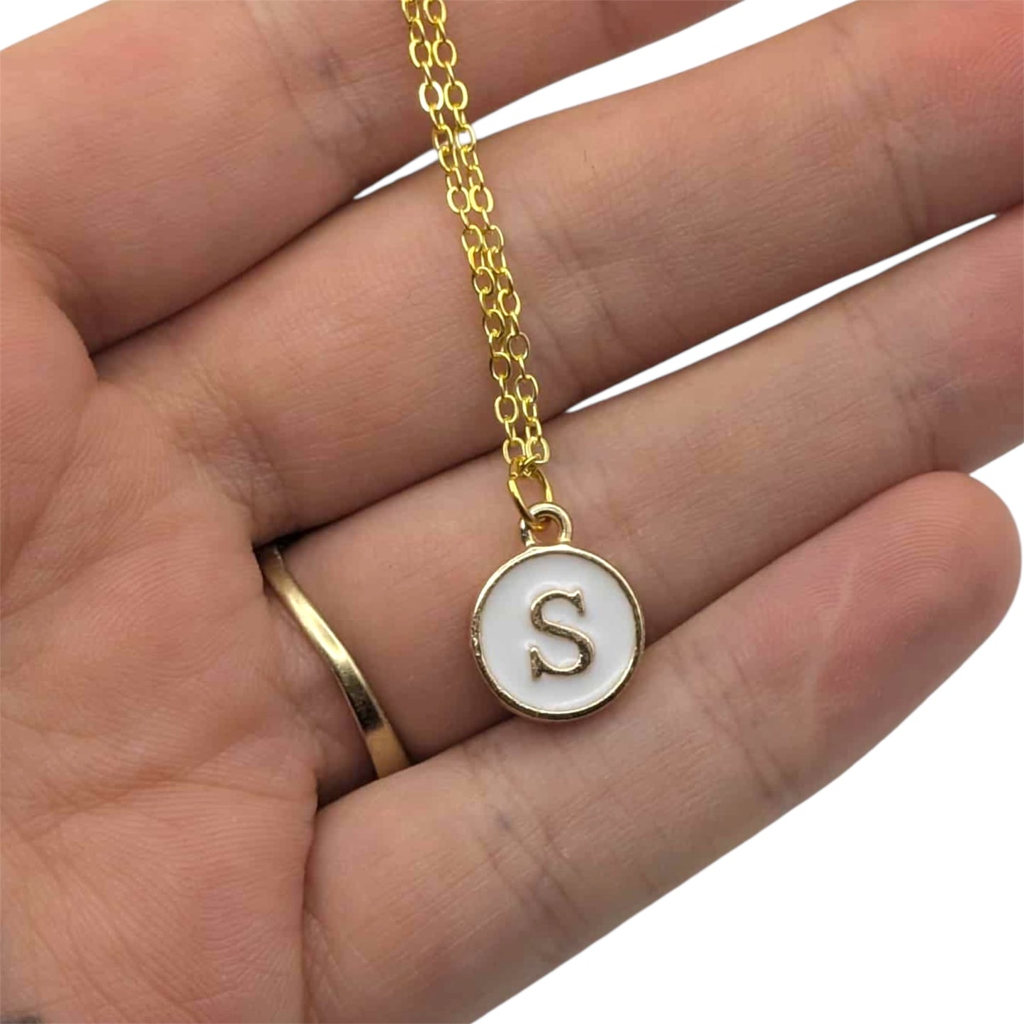 Gold necklace with a pendant featuring the letter 'S' held in a hand.