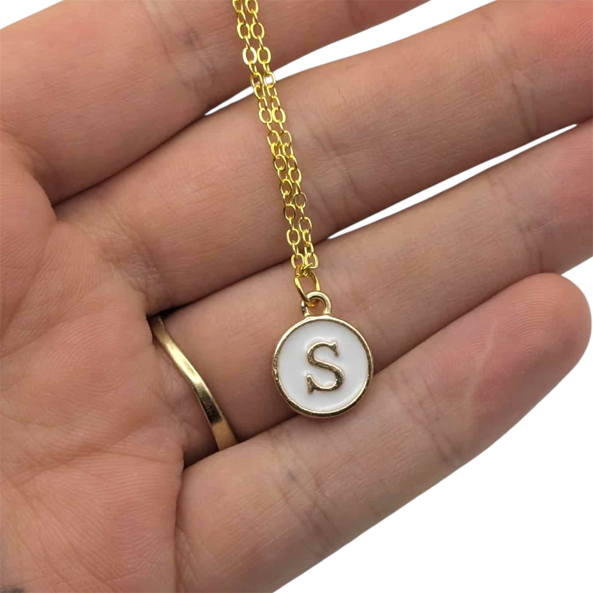 Gold necklace with a pendant featuring the letter 'S' held in a hand.