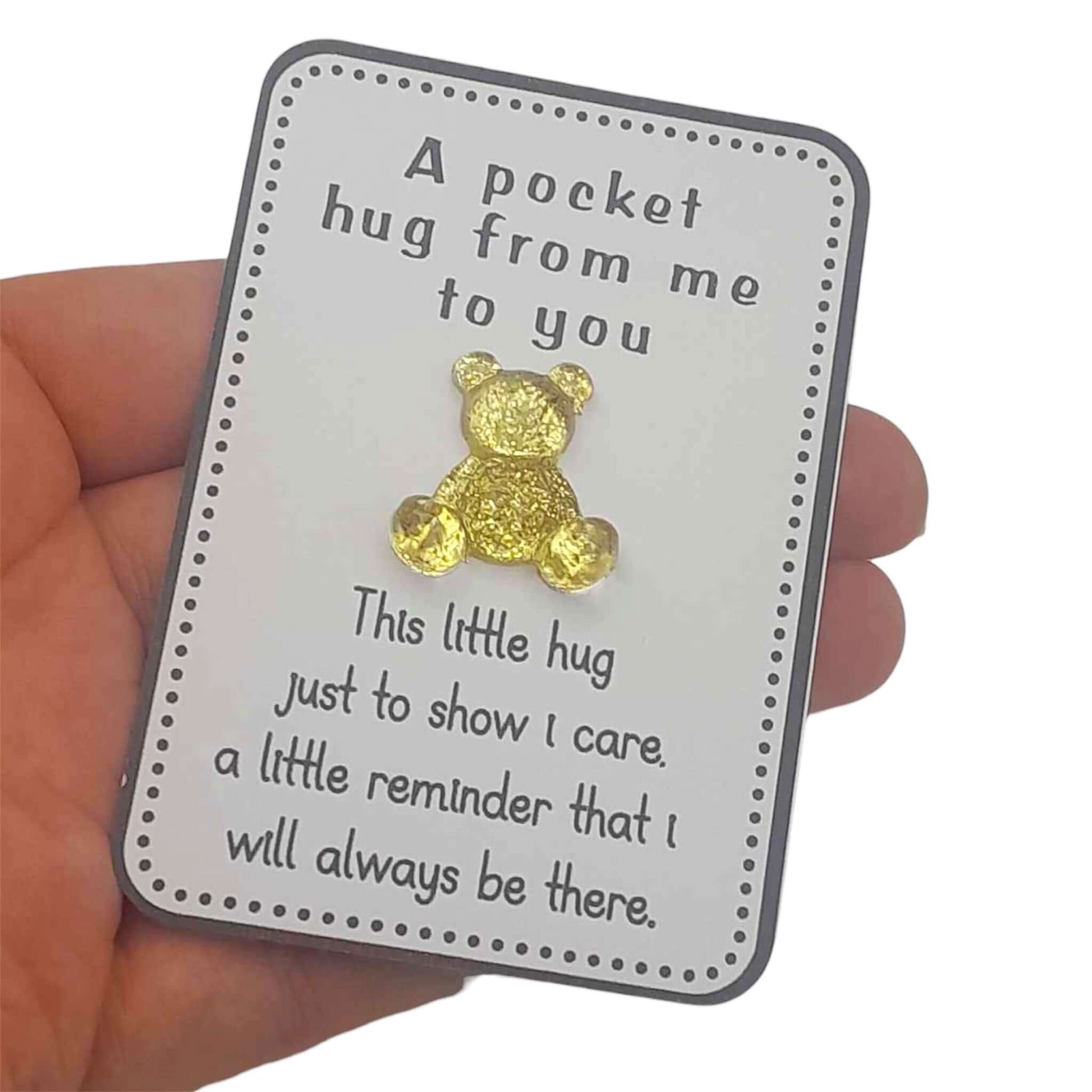 Gold teddy bear on a card with text, held in a hand.