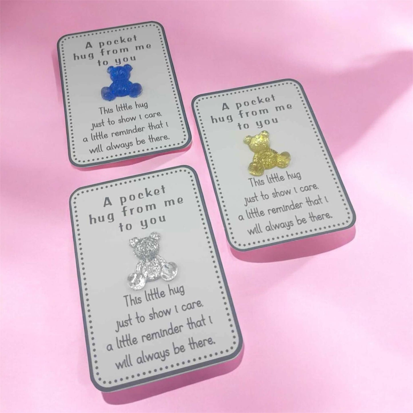 Three small rectangular cards with teddy bear pocket hugs and text on a pink background