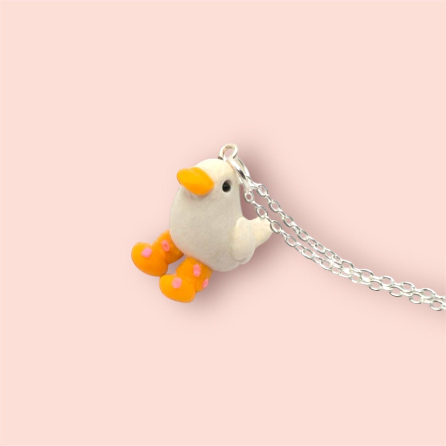 Small white bird charm with orange beak and feet on a pink background