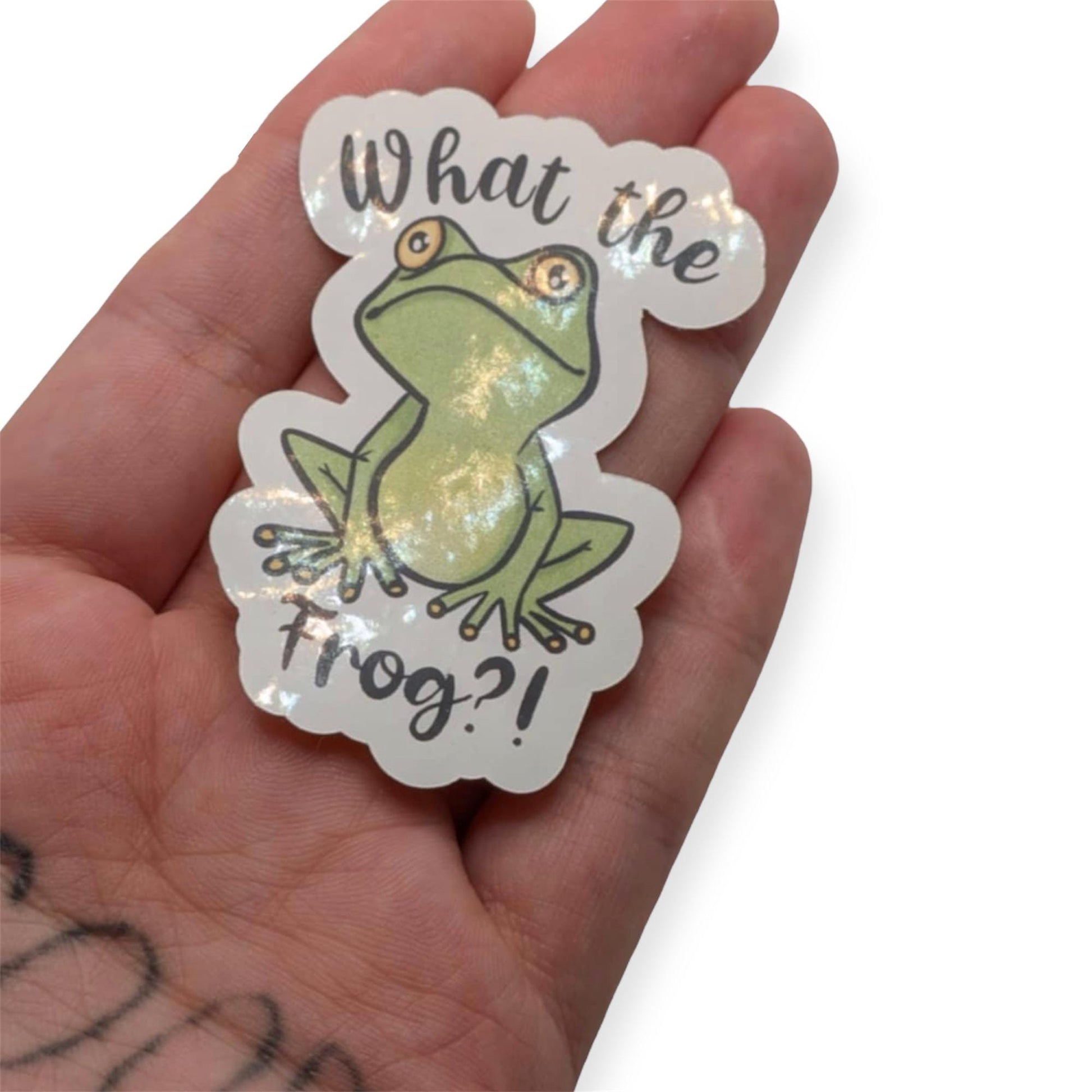 Sticker with a frog design and text held in a hand