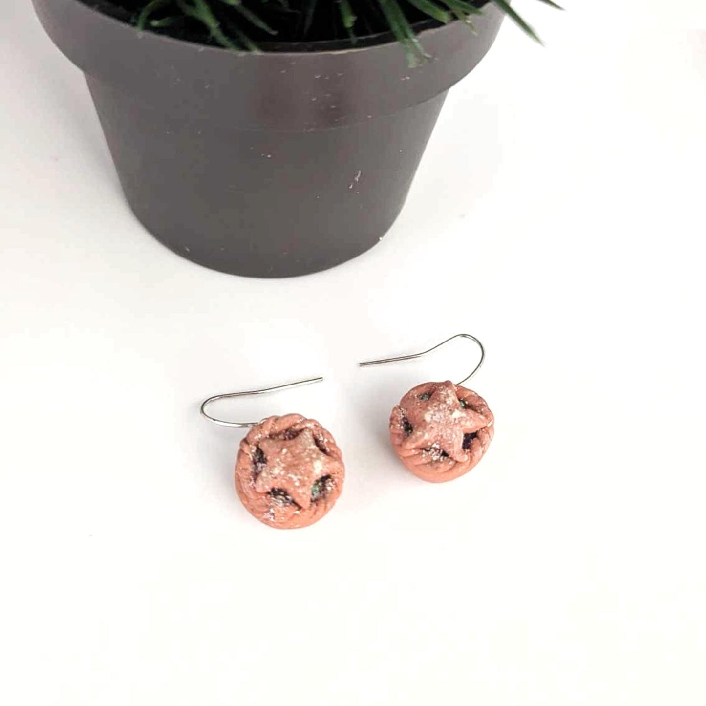 earrings on a white surface with a potted plant in the background