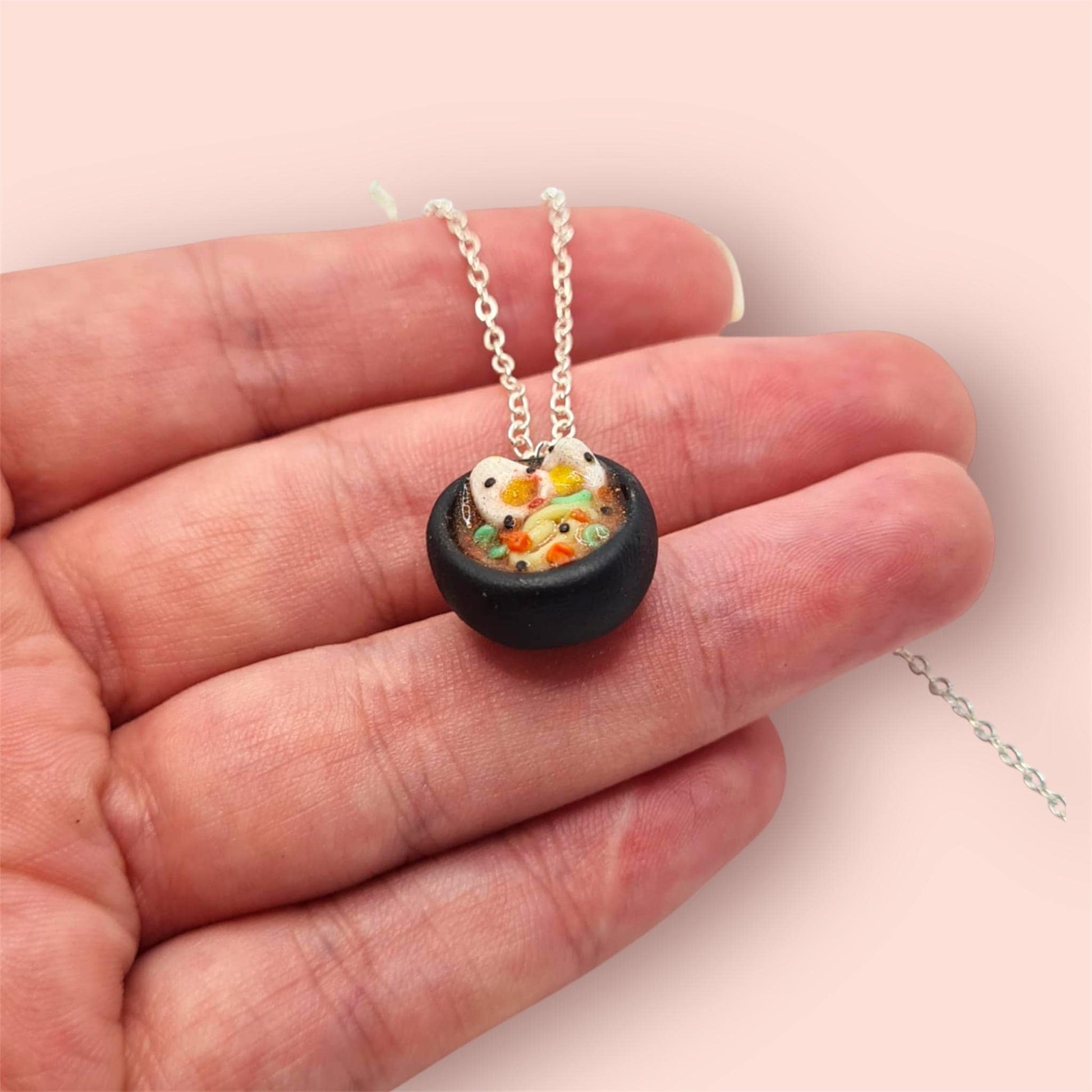 Noodle necklace held over hand with silver chain on light pink background 