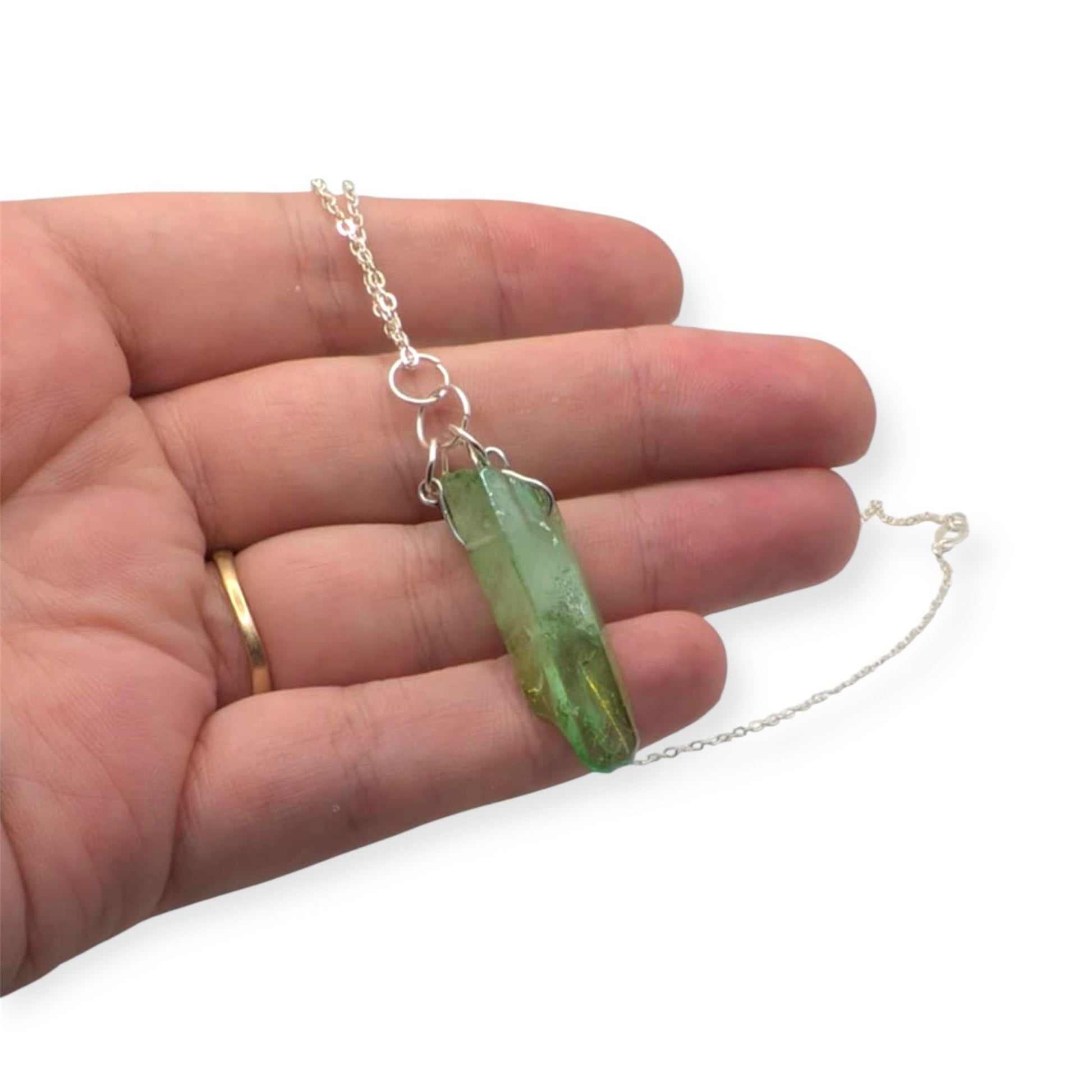 Hand holding a silver necklace with a green crystal pendant on a white background