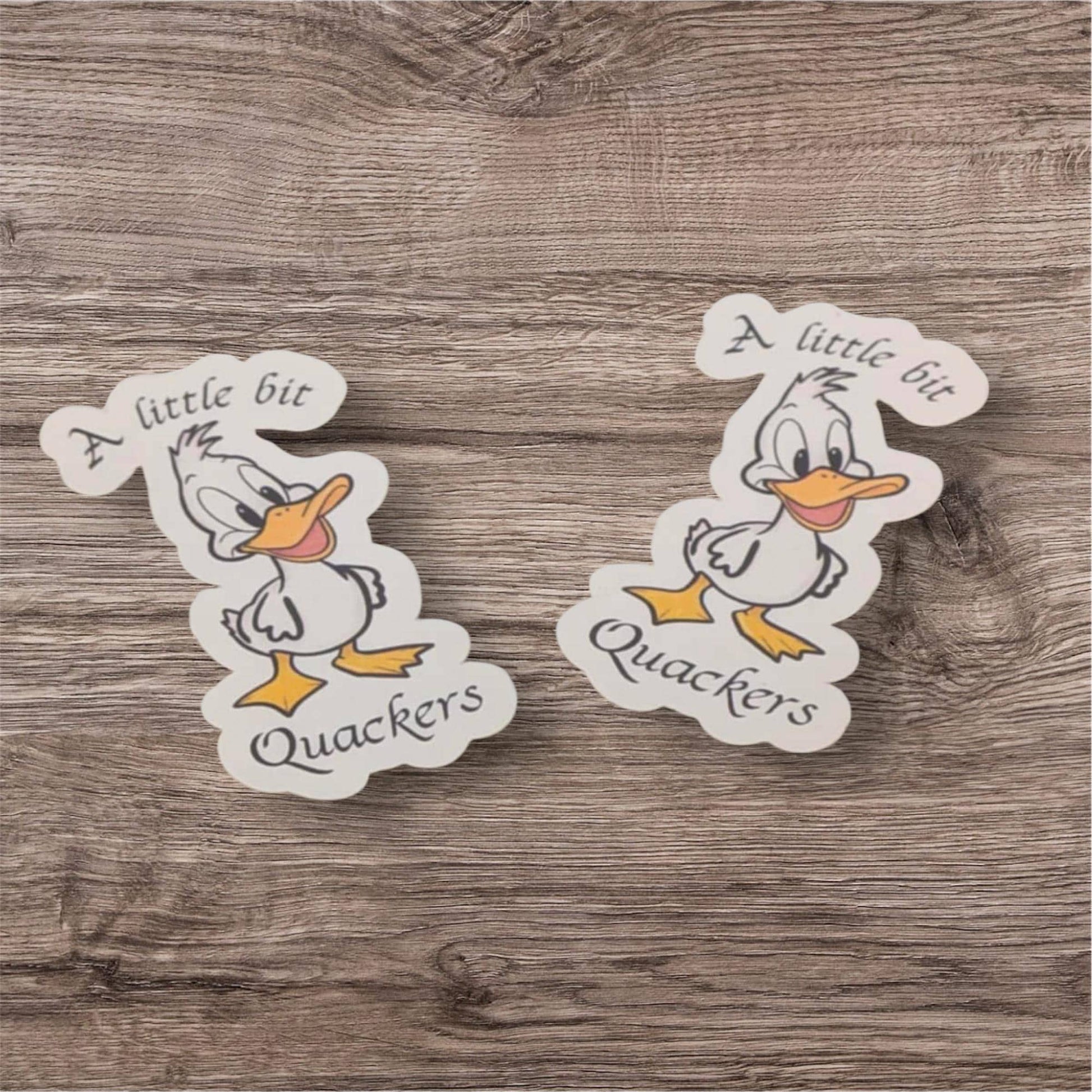Two cartoon duck stickers with text on a wooden surface