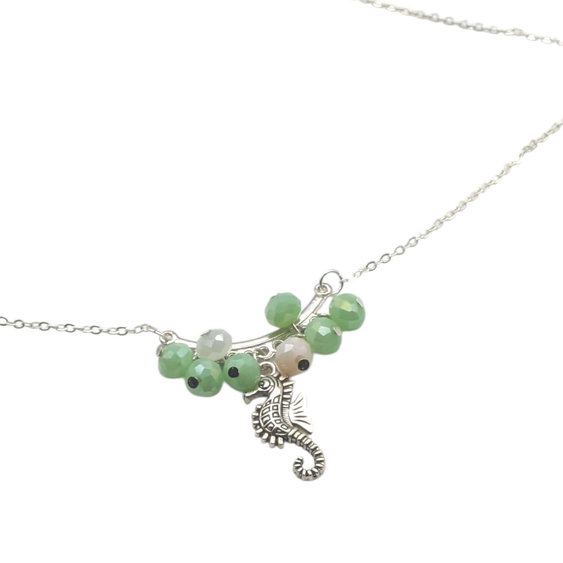 Silver chain seahorse necklace with green and pink crystals on white background 