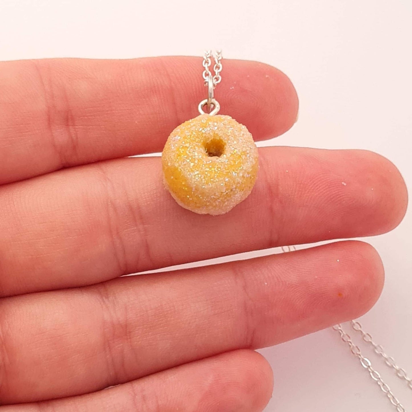 Donut-shaped pendant on a chain held between fingers against a white background