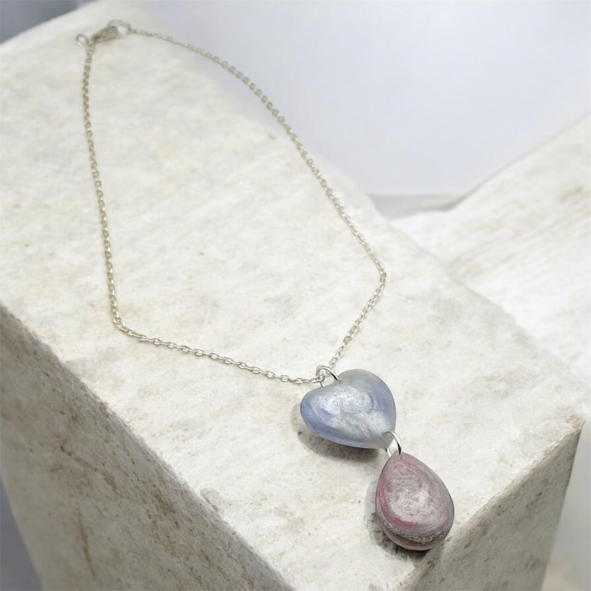 Pearl coloured heart and tear drop necklace with silver chain on a stone background