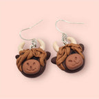 Highland cow-shaped earrings on a pink background