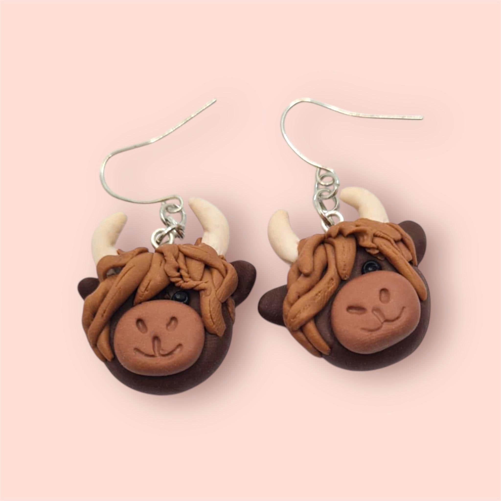 Highland cow-shaped earrings on a pink background