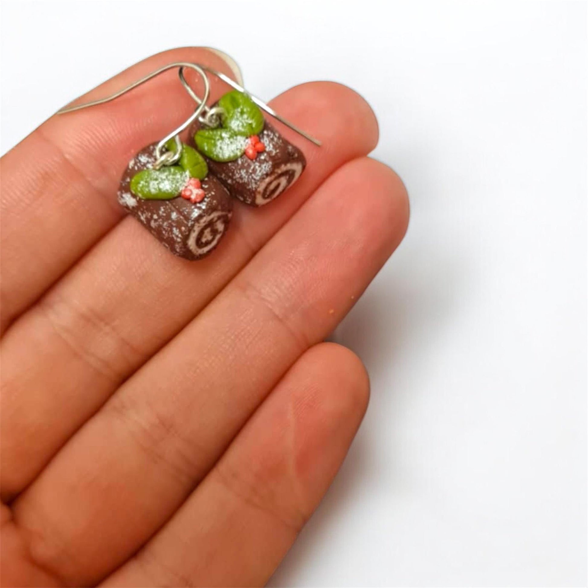 Earrings shaped like small pastries held between fingers on a white background