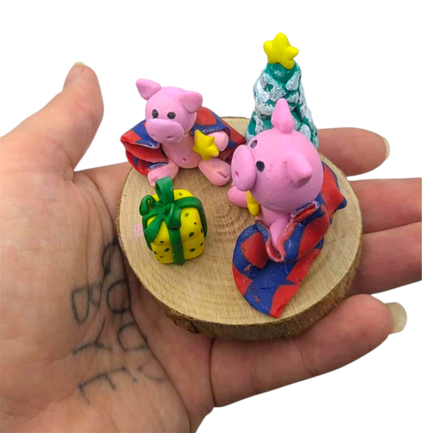 Hand holding a small wooden round base with colorful pig figurines and decorative items.